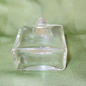 May include: A clear glass bottle with a square shape and a rounded top. The bottle is empty and has a smooth surface.