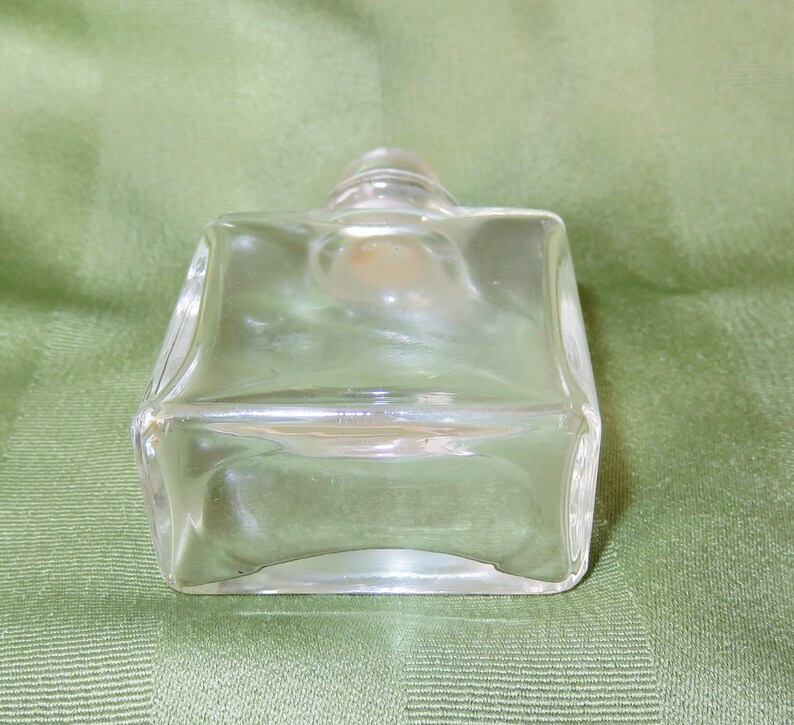 May include: A clear glass bottle with a square shape and a rounded top. The bottle is empty and has a smooth surface.