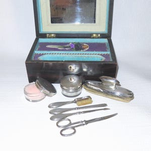 May include: A vintage wooden vanity set with a mirror, a small brush, a pair of scissors, a nail file, a small jar, and a silver-colored comb.