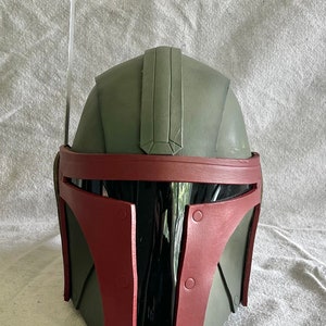 May include: A green and red Mandalorian helmet with a black visor and a black antenna on top.