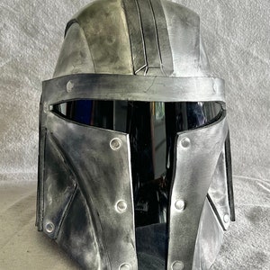 May include: A silver and black helmet with a visor and a weathered look. The helmet has a series of rivets around the edges.