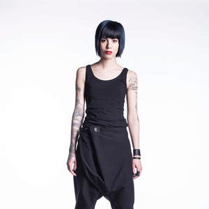 May include: A woman wearing a black tank top and black pants with a unique design. She has short, dark blue hair and tattoos on her arms.