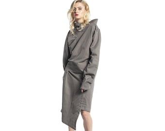 Puede incluir: Un vestido gris asimétrico con cuello alto y mangas largas. El vestido tiene una cintura ajustada y una falda fluida.
