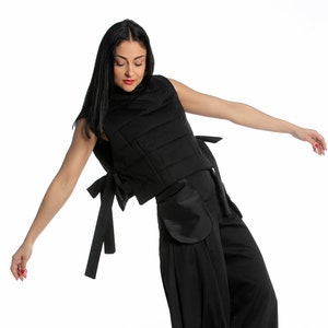 May include: A woman wearing a black sleeveless top with a quilted design and matching wide-leg trousers. The top has a bow detail at the back. She is wearing white trainers.