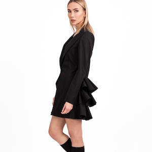 May include: A black blazer dress with a ruffled hem and long sleeves. The model is wearing black socks with the word "attitude" printed on them and black platform shoes.
