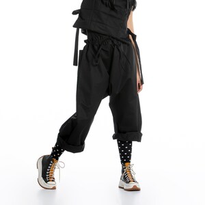 May include: A woman wearing a black quilted vest, black pants, and black and white polka dot socks. She is wearing black and white sneakers with a brown accent.