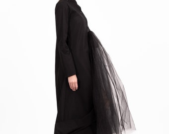 May include: A black long-sleeved dress with a tulle overlay. The dress has a high neckline and a button-up front. The model is wearing black shoes.