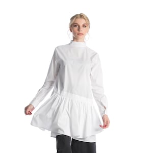 以下が含まれることがあります： ハイネックでフリルのある裾の白い長袖シャツ。シャツはダークブルーのワイドレッグパンツと黒のヒールブーツと組み合わせています。