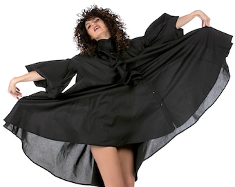 May include: A woman wearing a black, flowy dress with a ruffled collar and white sneakers. She is standing with her arms outstretched and the dress is billowing out around her.