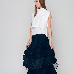 May include: A woman wearing a white sleeveless top and a black, ruffled skirt. The skirt is made of a sheer fabric and has a layered design.