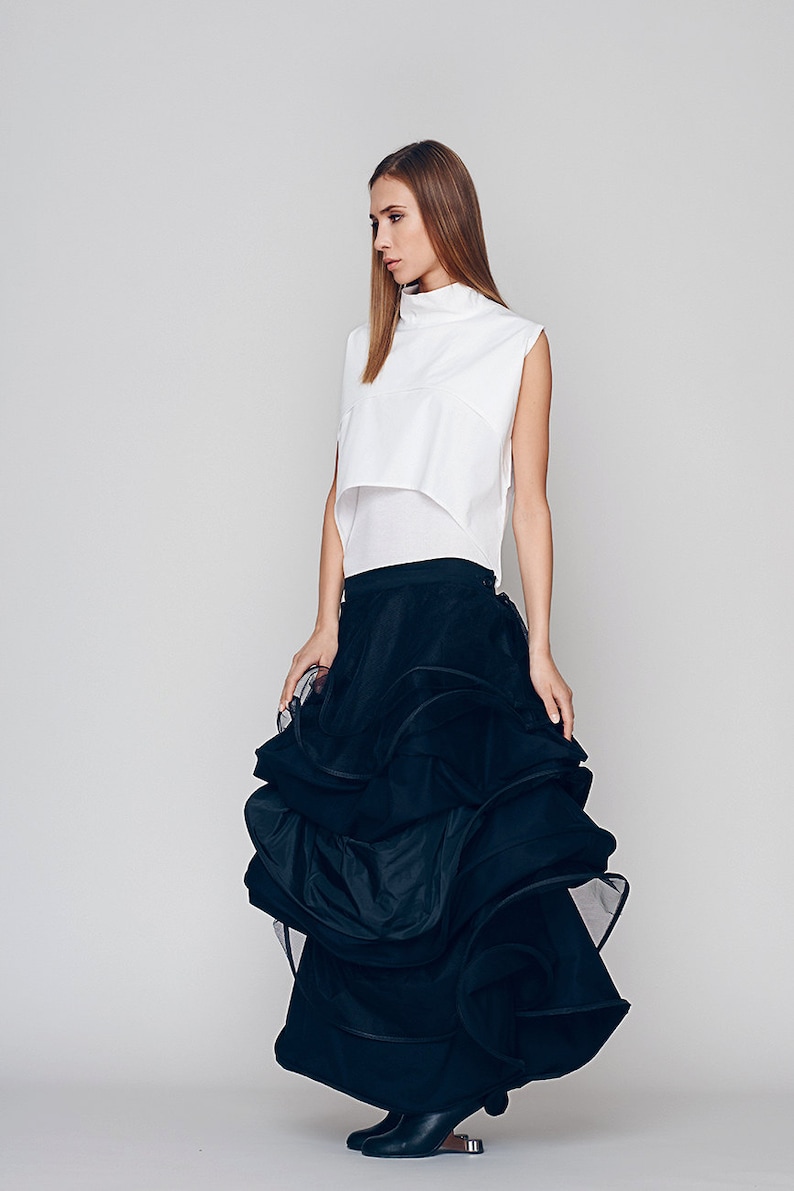 May include: A woman wearing a white sleeveless top and a black, ruffled skirt. The skirt is made of a sheer fabric and has a layered design.