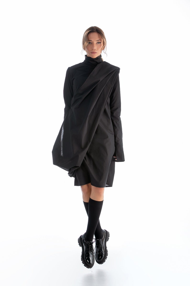 May include: A black long-sleeved dress with a draped neckline and a loose fit. The dress is worn with black socks and black leather shoes.