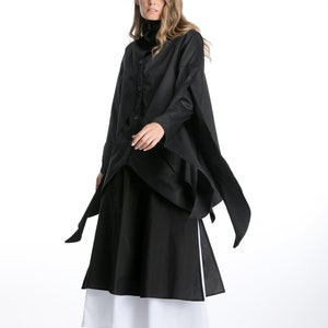 May include: A black long-sleeved shirt with a collar and a long, flowing skirt. The shirt has a unique design with a layered look and long ties that hang down the sides. The skirt is layered with a white underskirt.