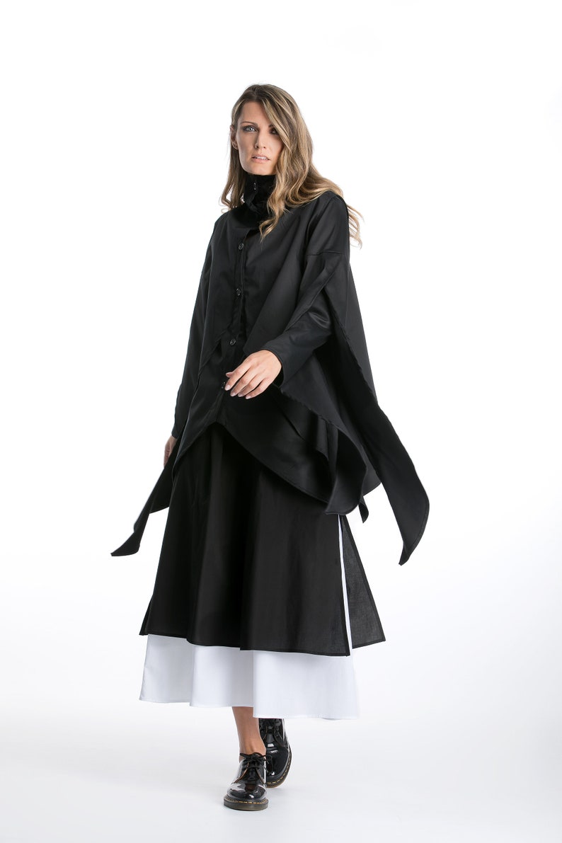 May include: A black long-sleeved shirt with a collar and a long, flowing skirt. The shirt has a unique design with a layered look and long ties that hang down the sides. The skirt is layered with a white underskirt.