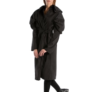 May include: A black long-sleeved coat with a belted waist and puffed sleeves. The coat is being worn by a person with blonde hair and is standing on a white background.
