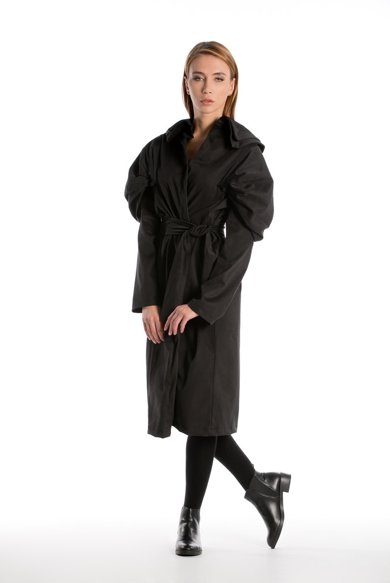 May include: A black long-sleeved coat with a belted waist and puffed sleeves. The coat is being worn by a person with blonde hair and is standing on a white background.