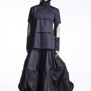May include: A black, layered, short-sleeved top with a high neck and a black, flowing skirt. The model is wearing black shoes.