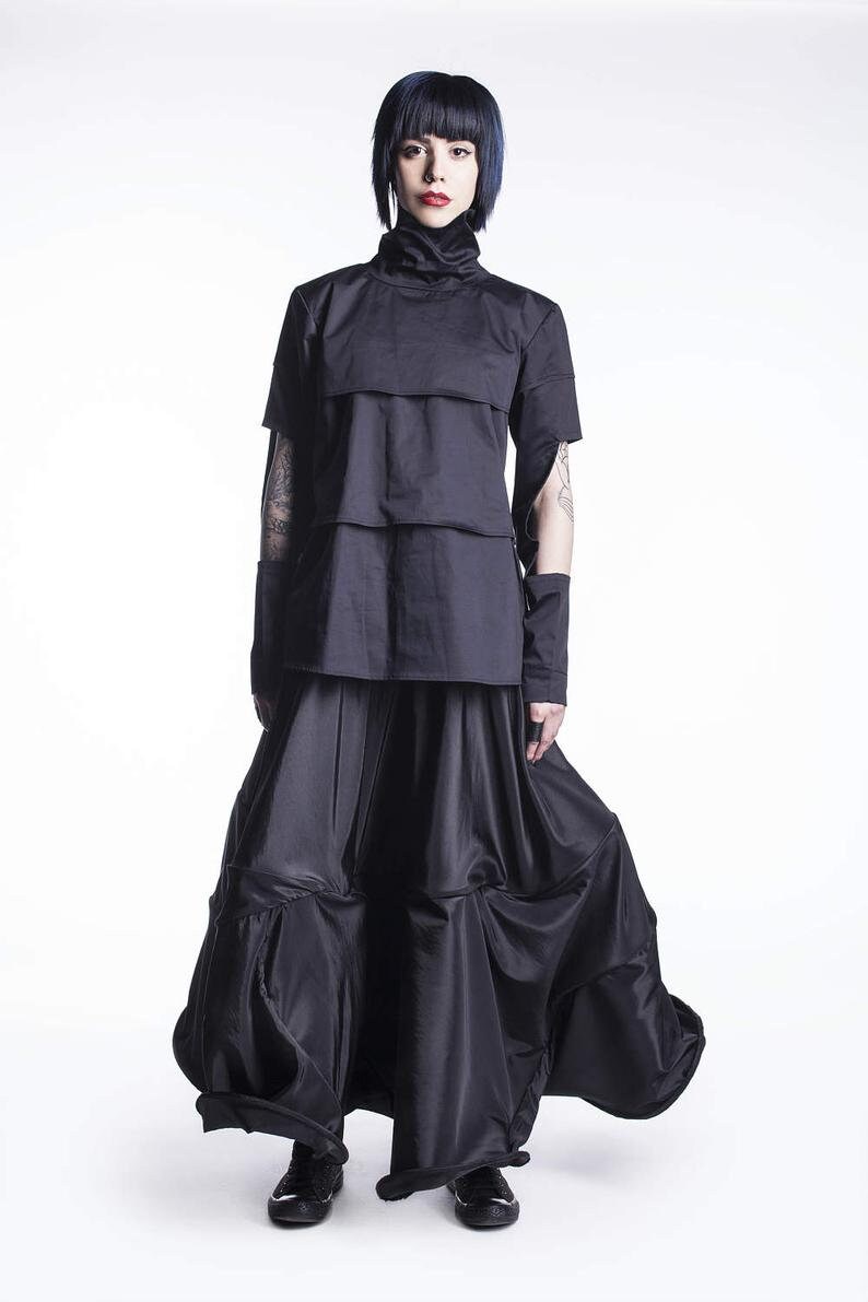 May include: A black, layered, short-sleeved top with a high neck and a black, flowing skirt. The model is wearing black shoes.