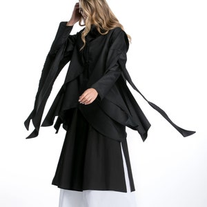 May include: A black long-sleeved shirt with a layered design and long, flowing sleeves. The shirt is paired with a black and white skirt.