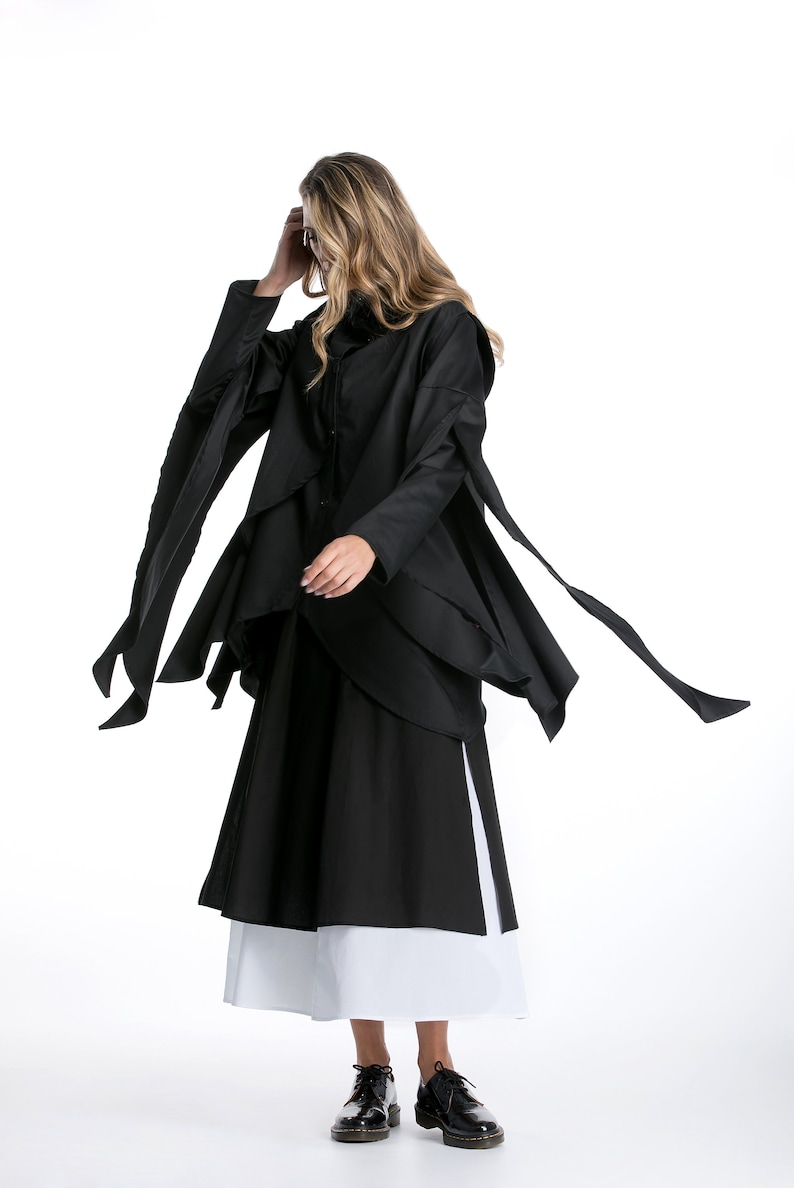 May include: A black long-sleeved shirt with a layered design and long, flowing sleeves. The shirt is paired with a black and white skirt.