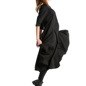 K&ouml;nnte beinhalten: Eine Frau in einem schwarzen Kleid mit wallendem Rock springt in der Luft. Sie tr&auml;gt schwarze Stiefel und hat ihre Haare nach hinten gebunden.