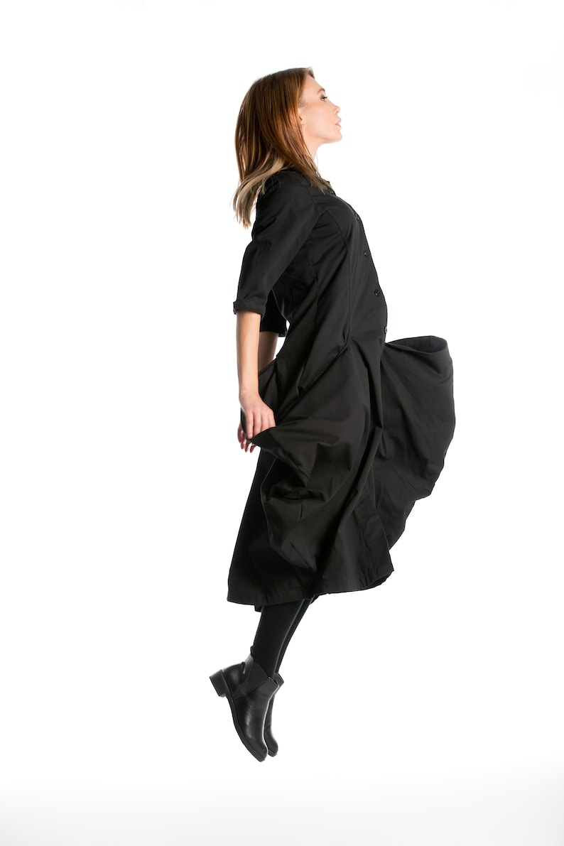 K&ouml;nnte beinhalten: Eine Frau in einem schwarzen Kleid mit wallendem Rock springt in der Luft. Sie tr&auml;gt schwarze Stiefel und hat ihre Haare nach hinten gebunden.