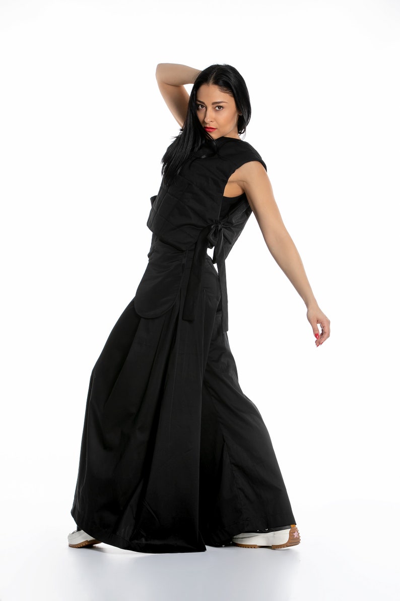 May include: A woman wearing a black sleeveless top and wide-legged trousers. The top has a tie at the back and the trousers have a wide, flowing silhouette.