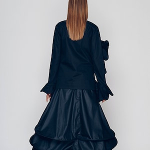May include: A black long-sleeved blouse with ruffled cuffs and a black tiered skirt. The skirt has multiple layers of fabric that create a voluminous silhouette.