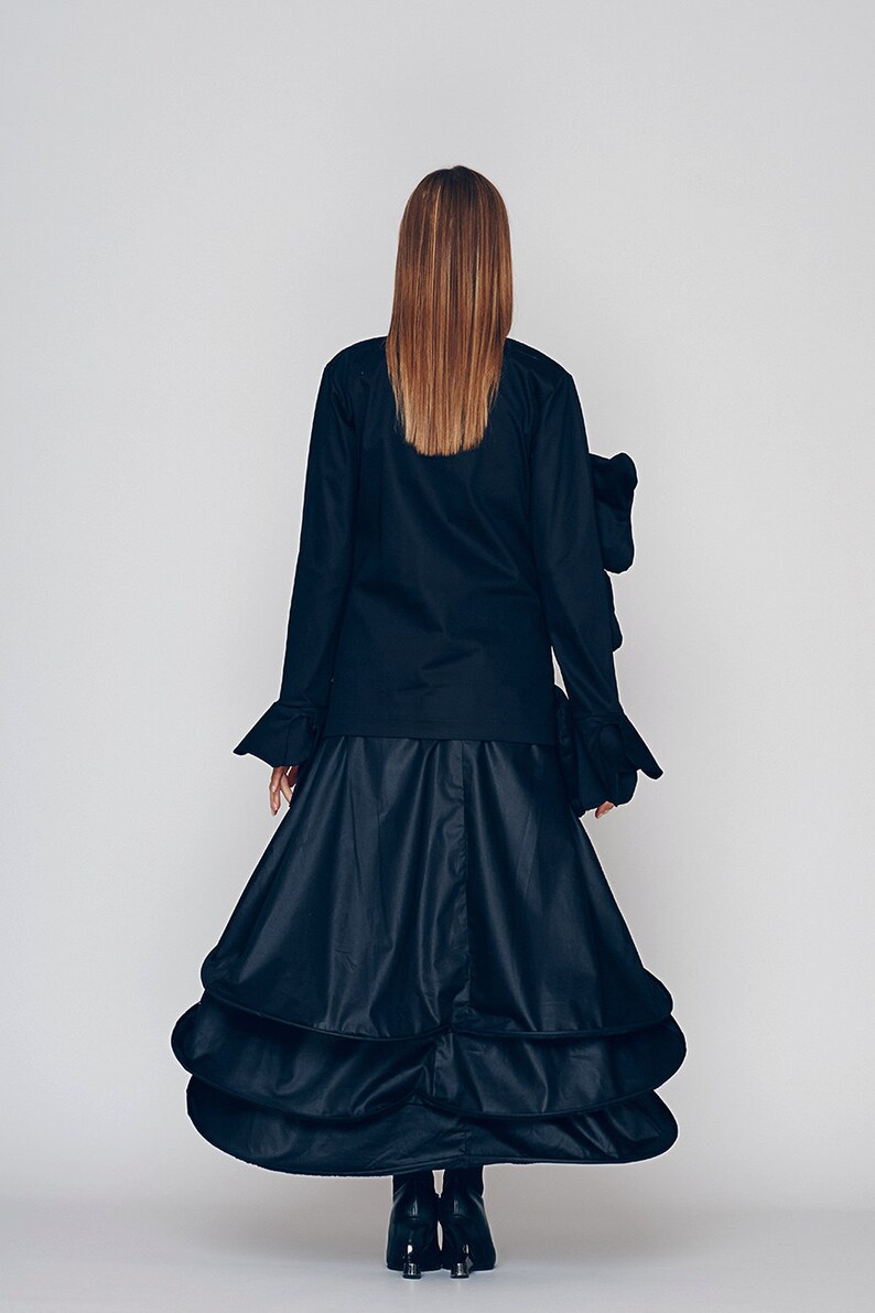 May include: A black long-sleeved blouse with ruffled cuffs and a black tiered skirt. The skirt has multiple layers of fabric that create a voluminous silhouette.