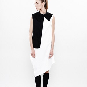 May include: A woman wearing a white and black sleeveless dress with a black collar. She is wearing black socks and black boots.
