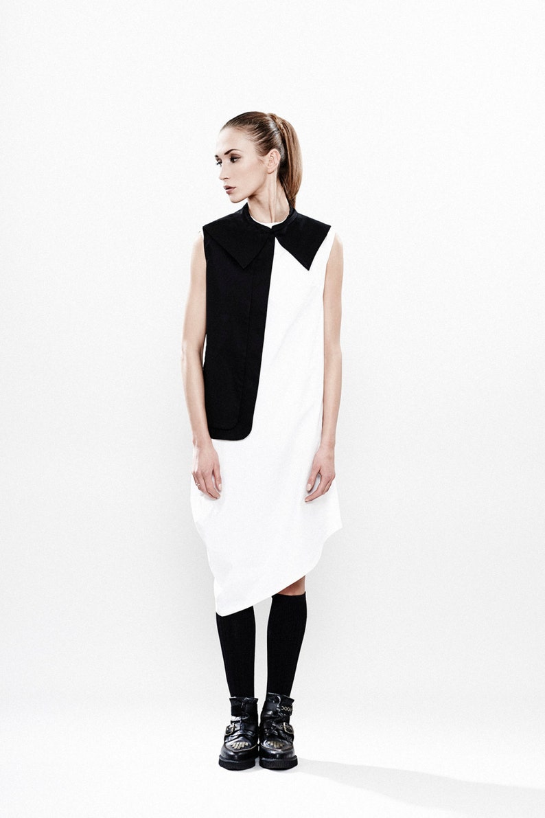 May include: A woman wearing a white and black sleeveless dress with a black collar. She is wearing black socks and black boots.