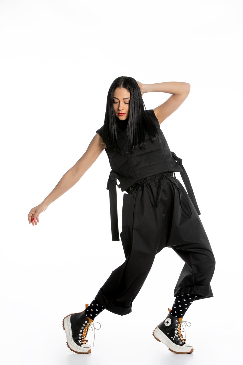 May include: A woman wearing a black sleeveless top with a quilted design and black pants. She is wearing black and white polka dot socks and black and white high-top sneakers with brown accents.