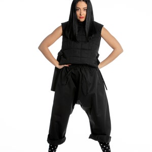 May include: A woman wearing a black quilted vest, black trousers with a drawstring waist, black and white polka dot socks, and black and white trainers with orange accents.