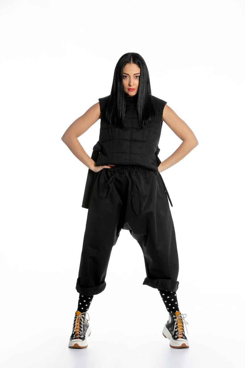 May include: A woman wearing a black quilted vest, black trousers with a drawstring waist, black and white polka dot socks, and black and white trainers with orange accents.