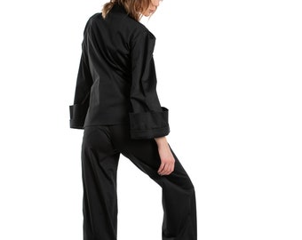 May include: A black pantsuit with long sleeves and wide legs. The pants and jacket have wide cuffs. The model is wearing black shoes.