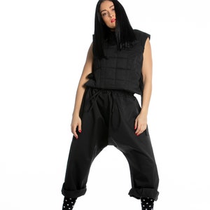 May include: A woman wearing a black quilted vest, black pants, black and white polka dot socks, and black and white sneakers with a brown accent.