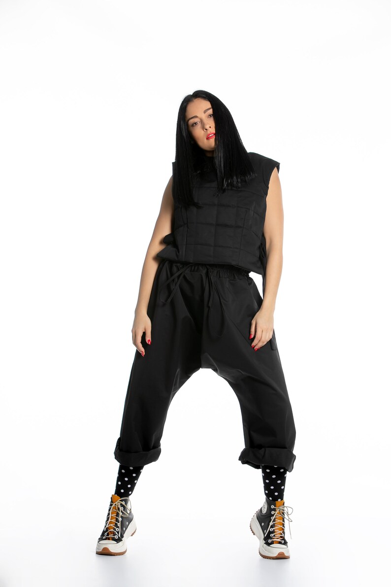 May include: A woman wearing a black quilted vest, black pants, black and white polka dot socks, and black and white sneakers with a brown accent.