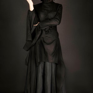 May include: A black long-sleeved dress with a high neck and a flowing skirt. The dress has a unique design with a layered skirt and a belt.