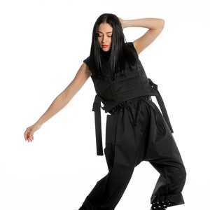 May include: A woman wearing a black sleeveless top with a quilted design and black trousers. She is wearing black and white polka dot socks and black and white high-top trainers with brown accents.