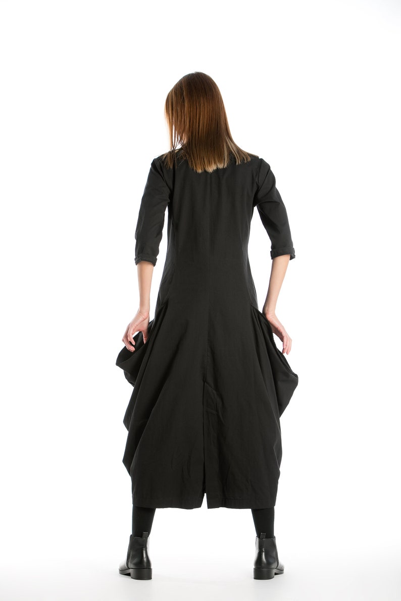 K&ouml;nnte beinhalten: Ein schwarzes, lang&auml;rmeliges Kleid mit einem flie&szlig;enden Rock und einem Schlitz im R&uuml;cken. Das Kleid wird von einer Person mit langen braunen Haaren getragen.