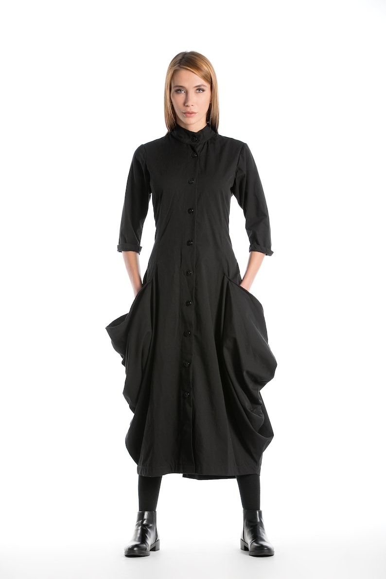 K&ouml;nnte beinhalten: Ein schwarzes, lang&auml;rmliges Kleid mit Knopfleiste und gro&szlig;en Taschen. Das Kleid hat eine lockere, flie&szlig;ende Passform und ist aus einem weichen, bequemen Stoff gefertigt.