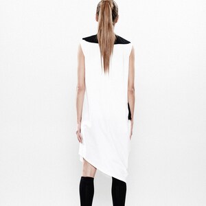 May include: A white sleeveless dress with a black collar and a black panel on the back. The dress has a loose fit and a slightly asymmetrical hemline. The model is wearing black knee-high socks and black shoes.