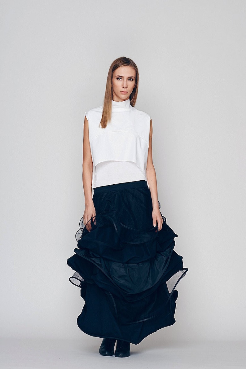 May include: A woman wearing a white sleeveless top and a black tiered skirt. The skirt is made of a sheer fabric and has multiple layers.