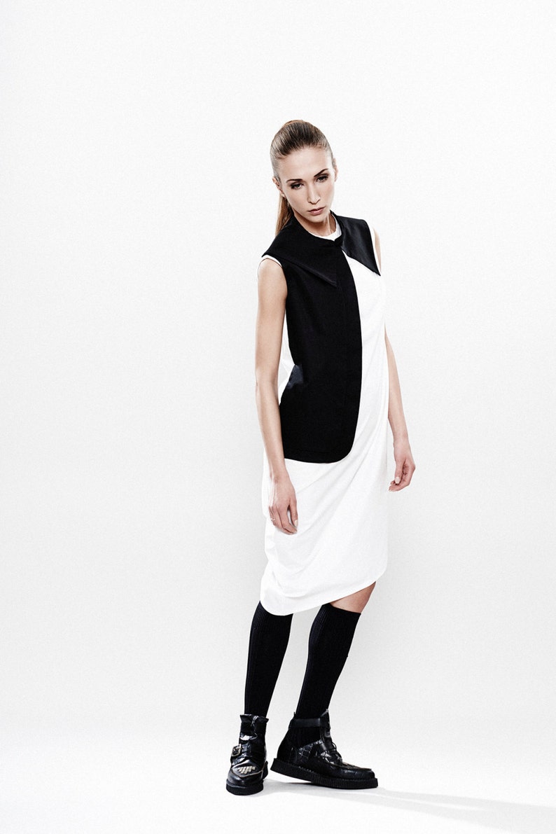 May include: A woman wearing a white dress with a black sleeveless vest. She is wearing black socks and black shoes.