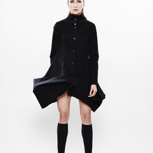 May include: A woman wearing a black, knee-length, collared dress with a button-up front. She is wearing black knee-high socks and black platform sandals.