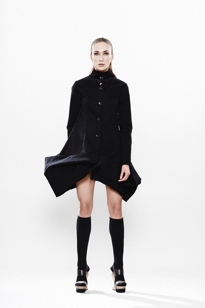 May include: A woman wearing a black, knee-length, collared dress with a button-up front. She is wearing black knee-high socks and black platform sandals.