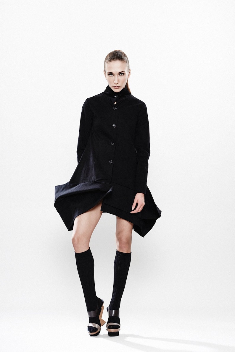 May include: A woman wearing a black long-sleeved dress with a button-up front and a high collar. She is wearing black knee-high socks and black platform sandals.