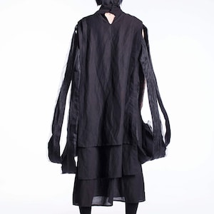 K&ouml;nnte beinhalten: Eine Person tr&auml;gt ein schwarzes, mehrschichtiges Kleid mit langen, flie&szlig;enden &Auml;rmeln. Das Kleid hat ein einzigartiges Design mit einem mehrschichtigen Rock und einem hohen Ausschnitt.