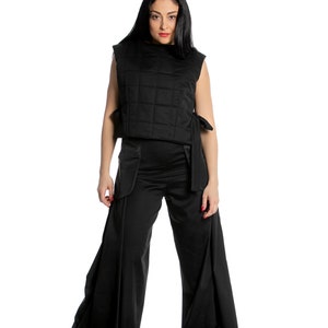 May include: A woman wearing a black quilted waistcoat and wide-leg trousers. The waistcoat has a tie at the waist and the trousers have a wide leg.