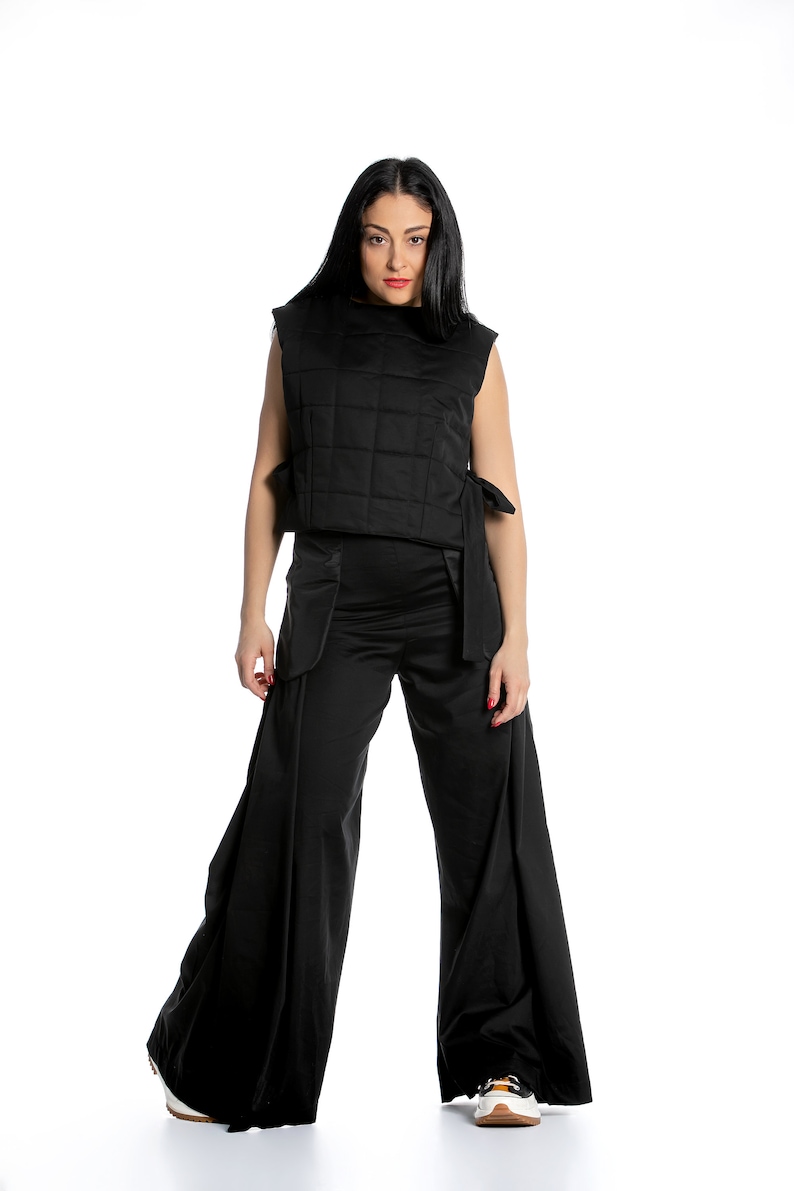 May include: A woman wearing a black quilted waistcoat and wide-leg trousers. The waistcoat has a tie at the waist and the trousers have a wide leg.